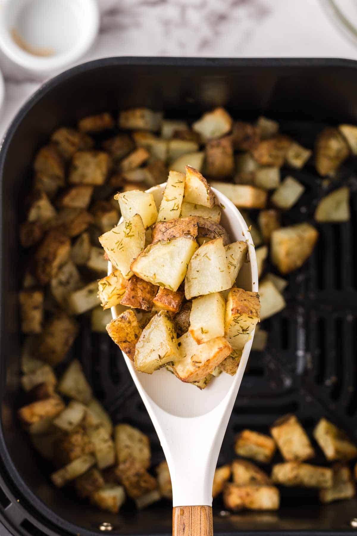 air fryer roasted potatoes on a big white spoon over the black air fryer basket.