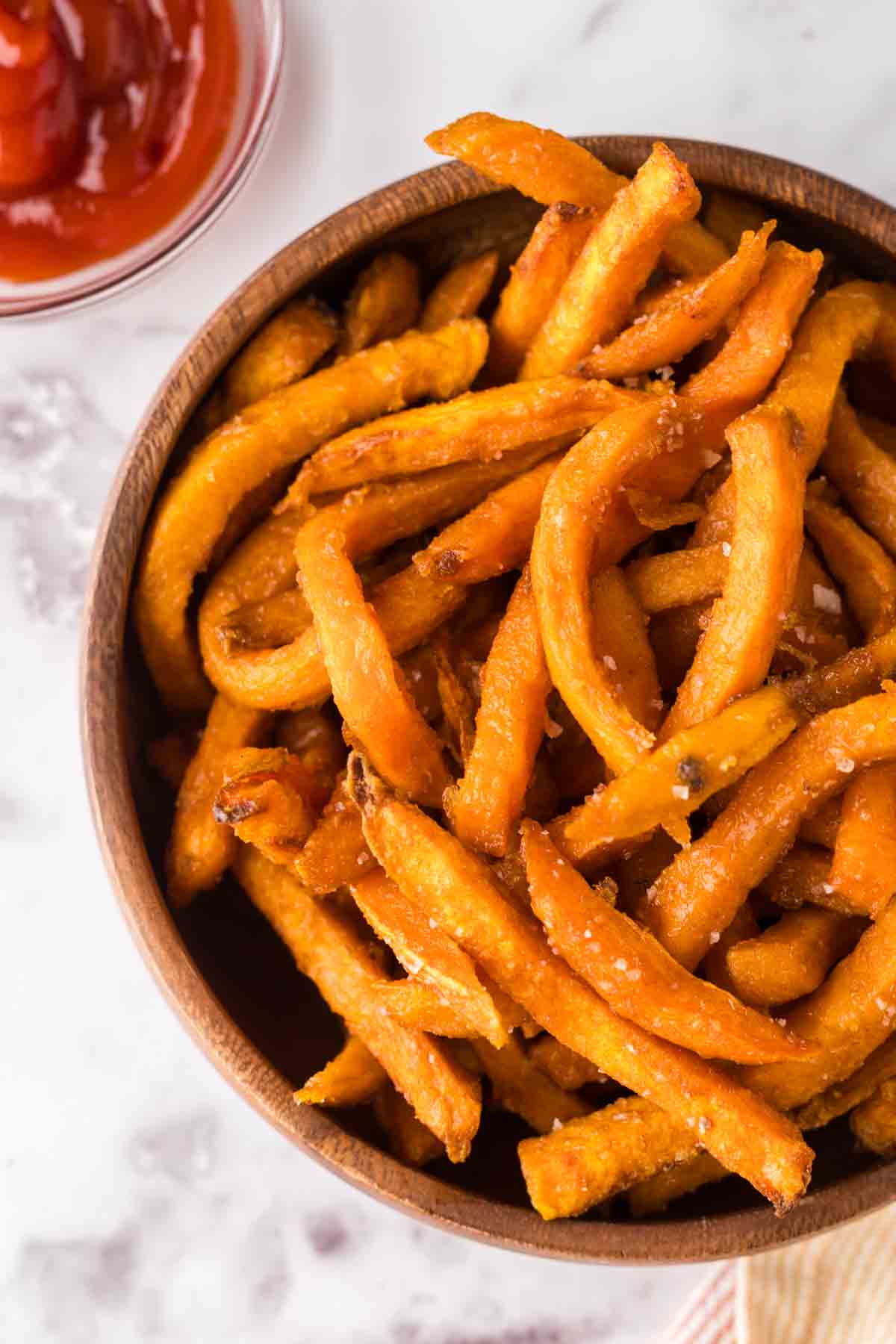 round wooden bowl with air fried sweet potato french fries with ketchup.