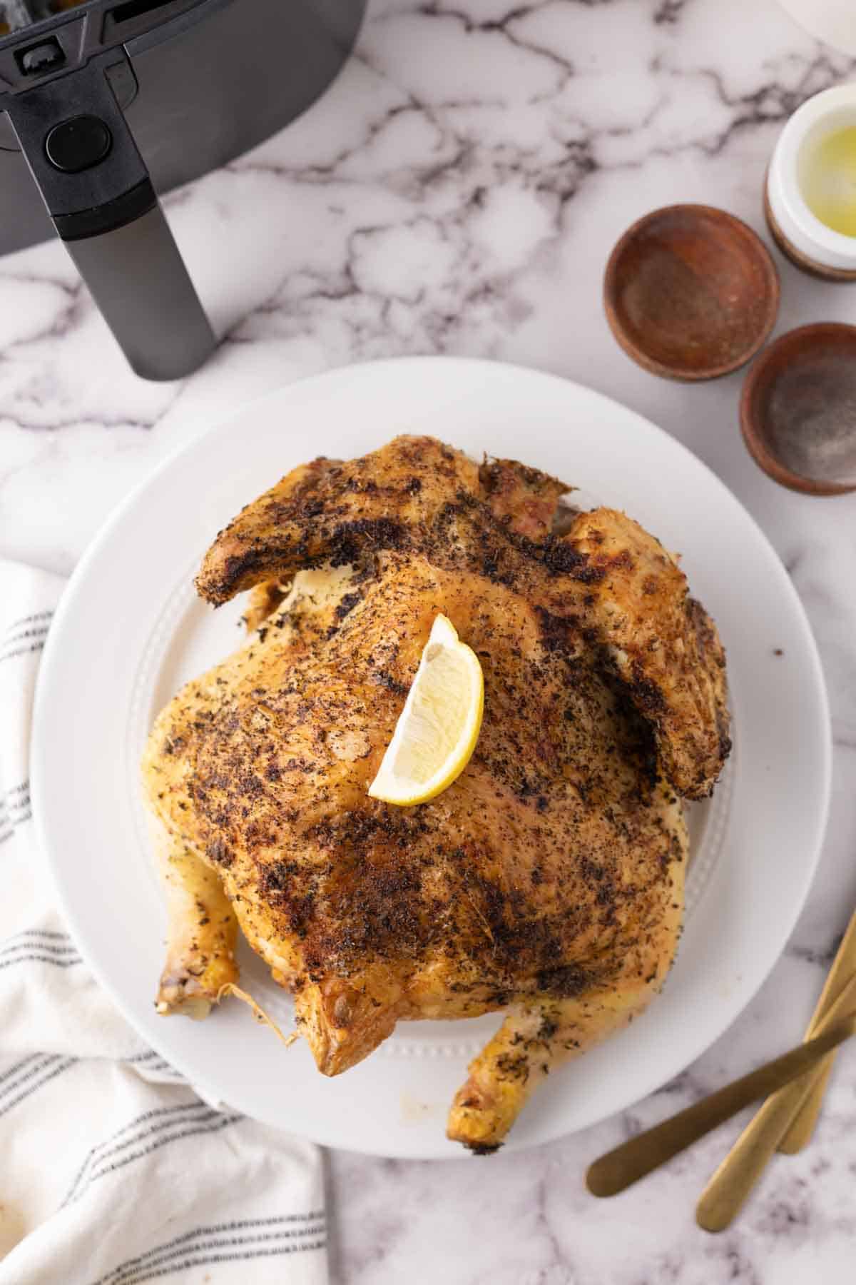 whole crispy skinned and seasoned air fryer chicken on a white plate.