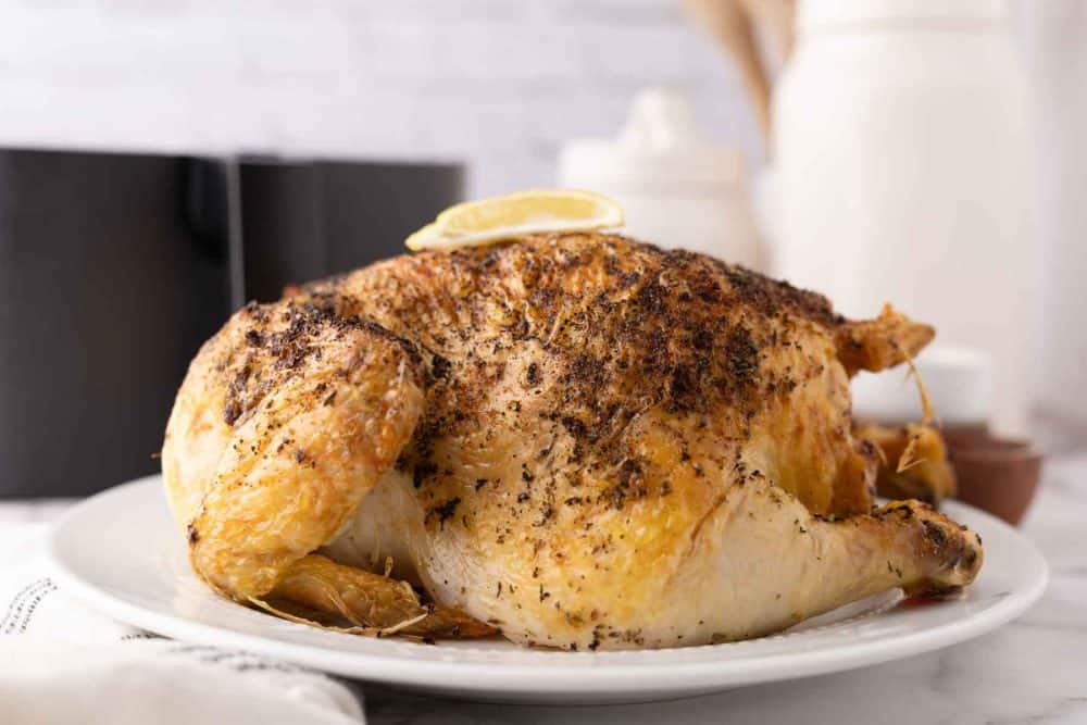 whole crispy skinned and seasoned air fryer chicken on a white plate.