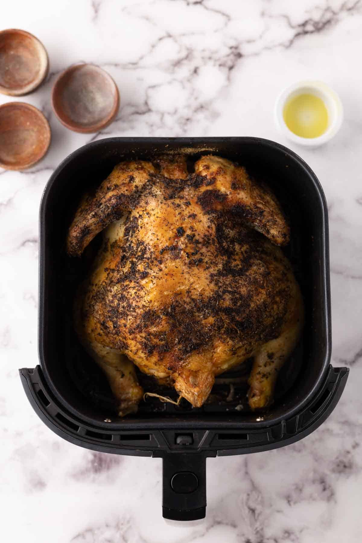 whole crispy skinned and seasoned air fryer chicken in a black air fryer basket.