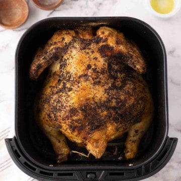 whole crispy skinned and seasoned air fryer chicken in a black air fryer basket.