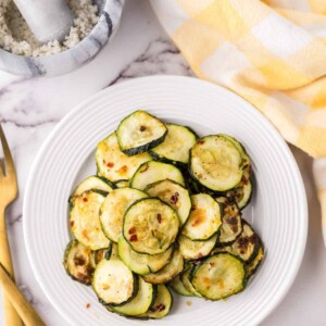 air fryer zucchini on a white plate with golden forks to the side.