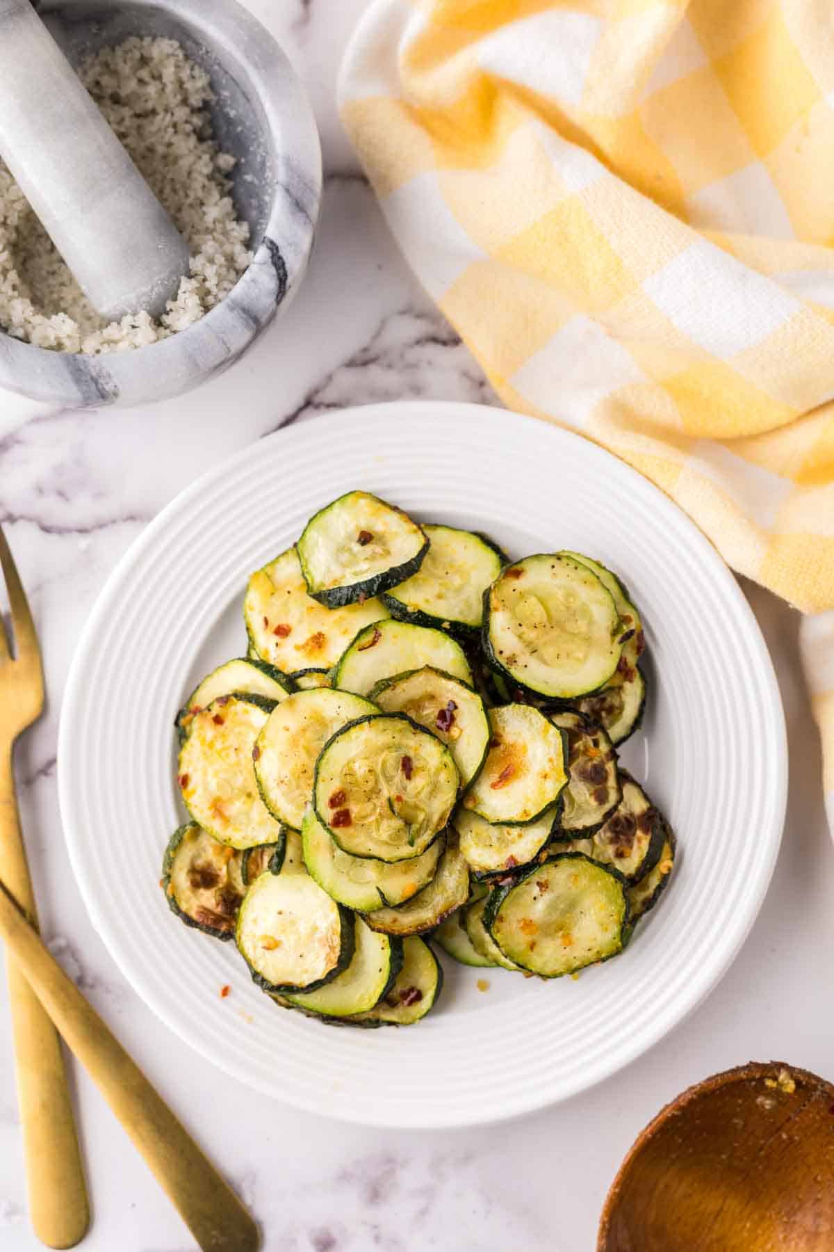 air fryer zucchini on a white plate with golden forks to the side.
