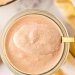 small glass jar of Alabama white sauce being spooned out with a golden spoon.