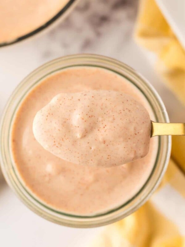 small glass jar of Alabama white sauce being spooned out with a golden spoon.