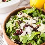 round wooden bowl with arugula salad with golden forks and lemons to the side.