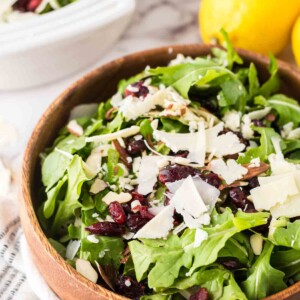 round wooden bowl with arugula salad with golden forks and lemons to the side.