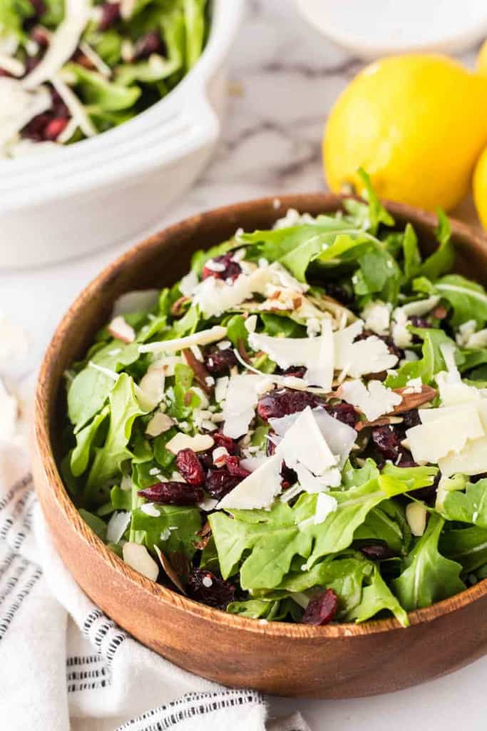 round wooden bowl with arugula salad with golden forks and lemons to the side.