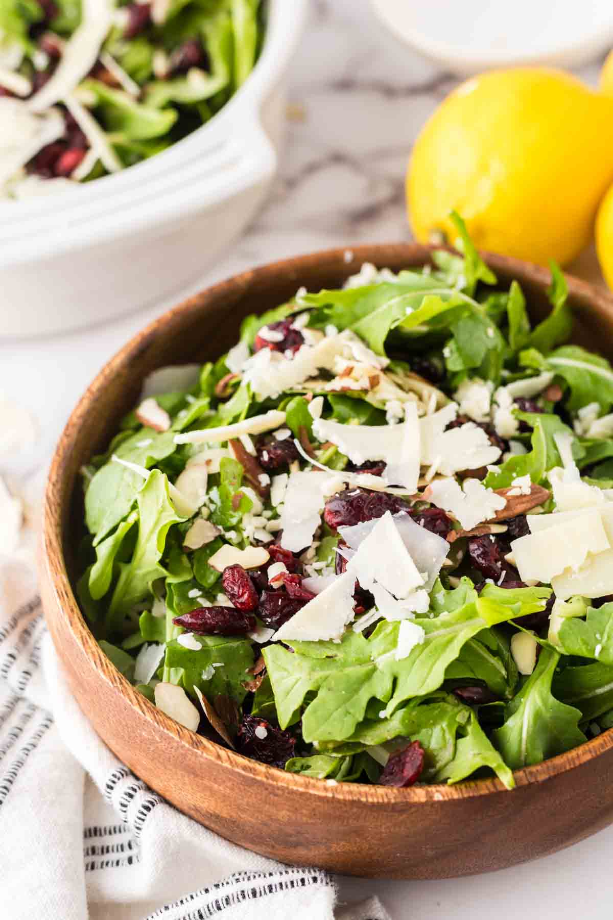 round wooden bowl with arugula salad with golden forks and lemons to the side.