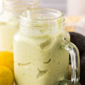 handled glass mason jar filled with avocado smoothie with fresh avocado lemon on the side.