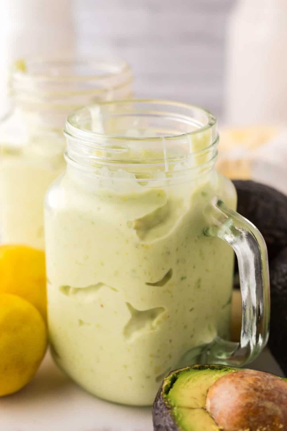 handled glass mason jar filled with avocado smoothie with fresh avocado lemon on the side.