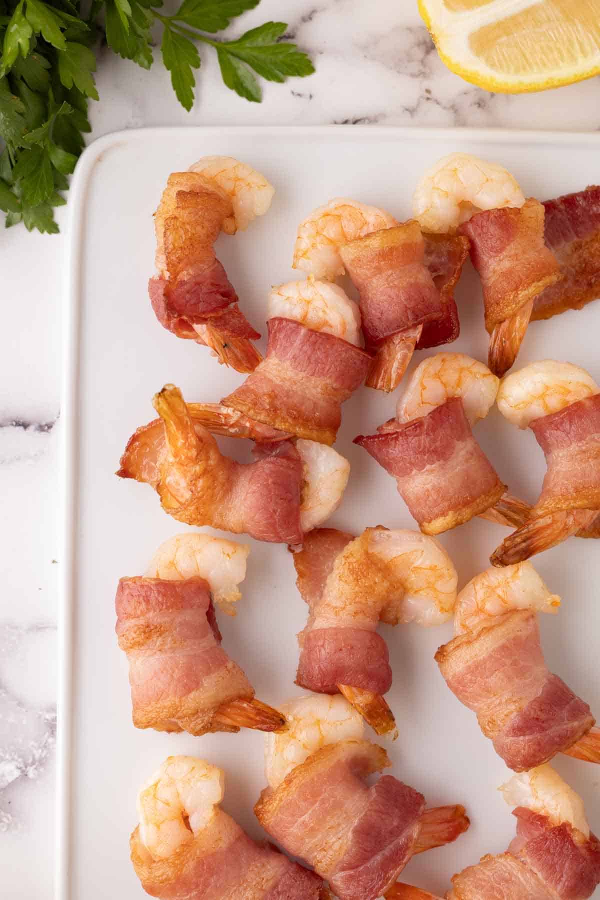 bacon wrapped shrimp recipe with lemons on a white cutting board paddle.