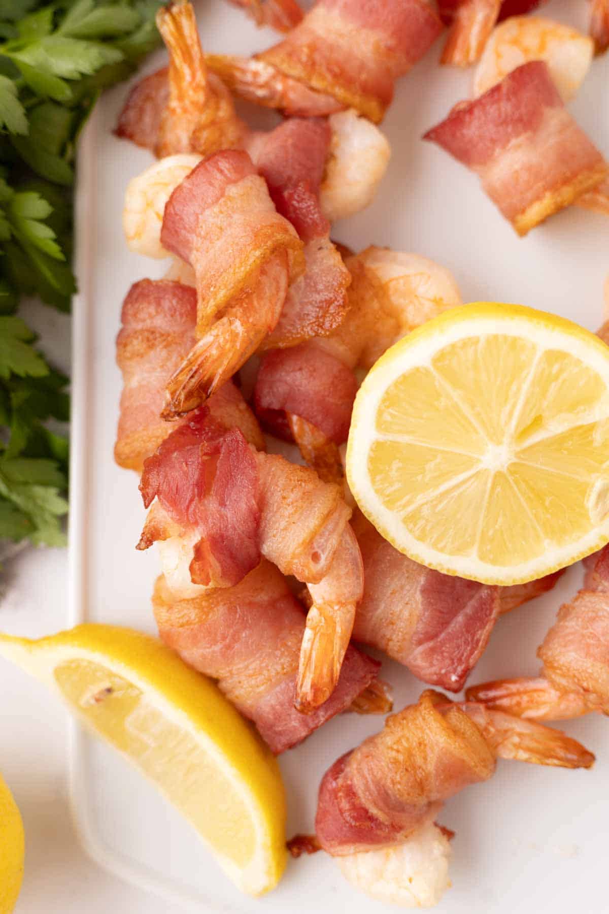 bacon wrapped shrimp recipe with lemons on a white cutting board paddle.