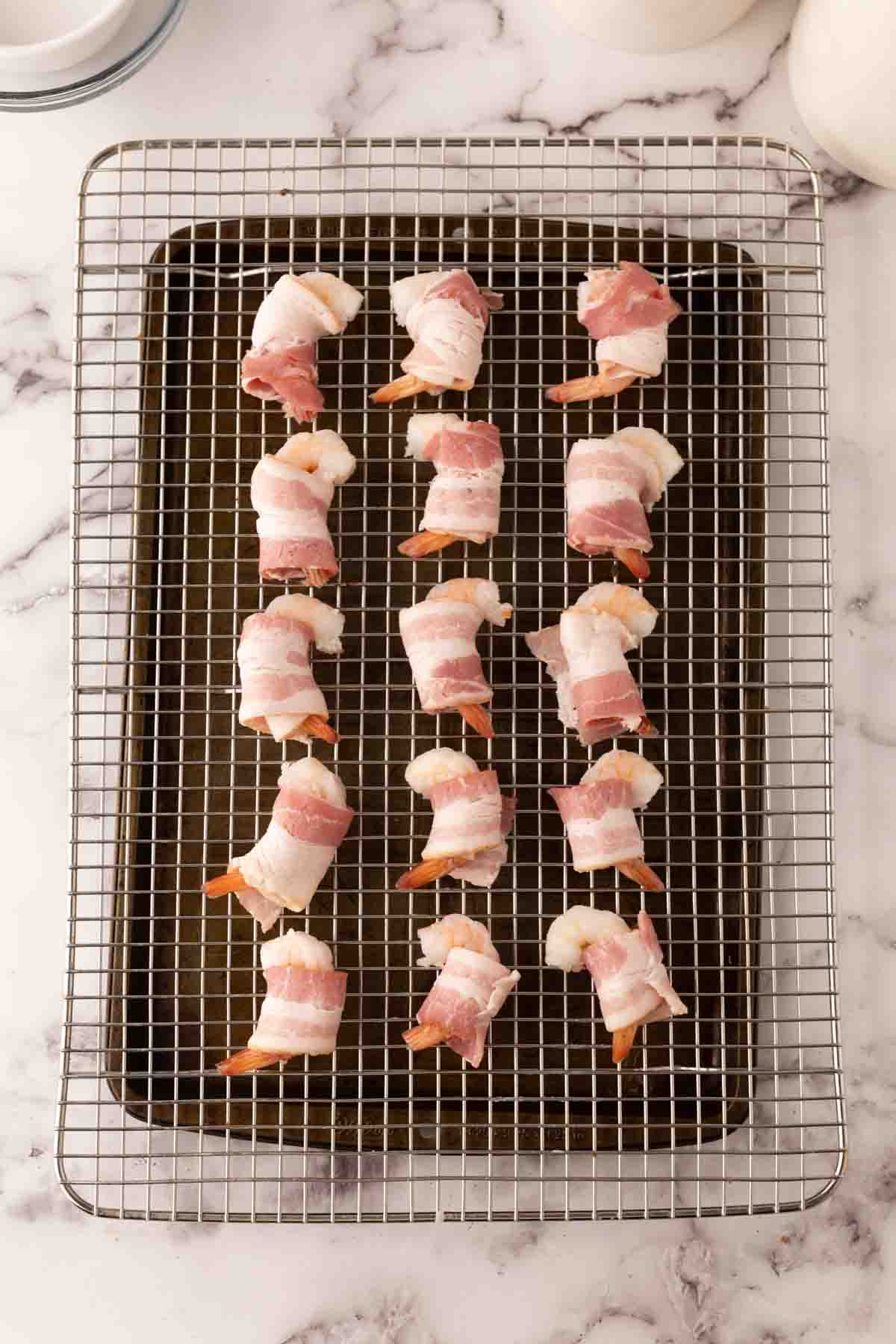 raw bacon wrapped shrimp on a tray over a baking dish.
