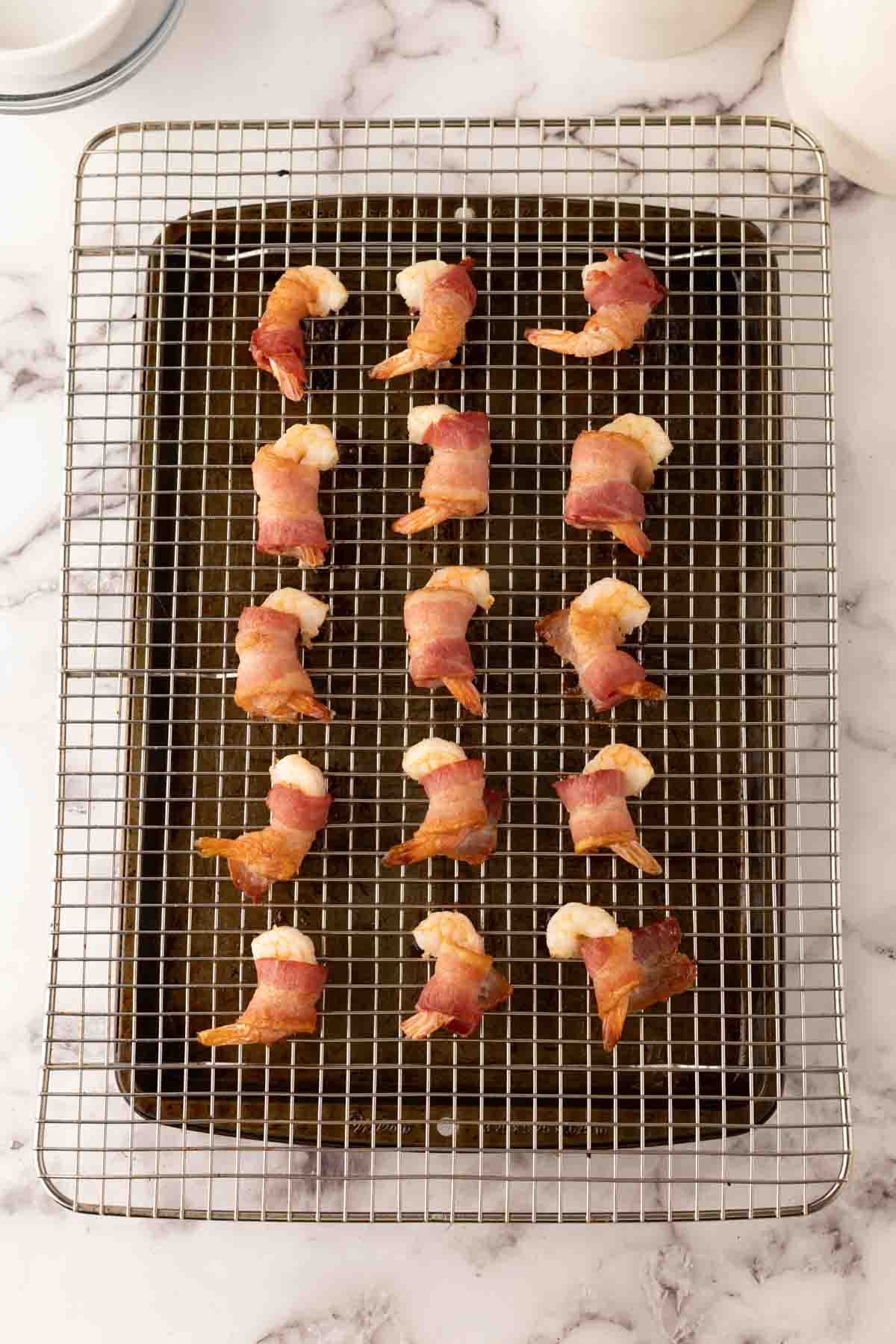 cooked bacon wrapped shrimp on a tray over a baking dish.