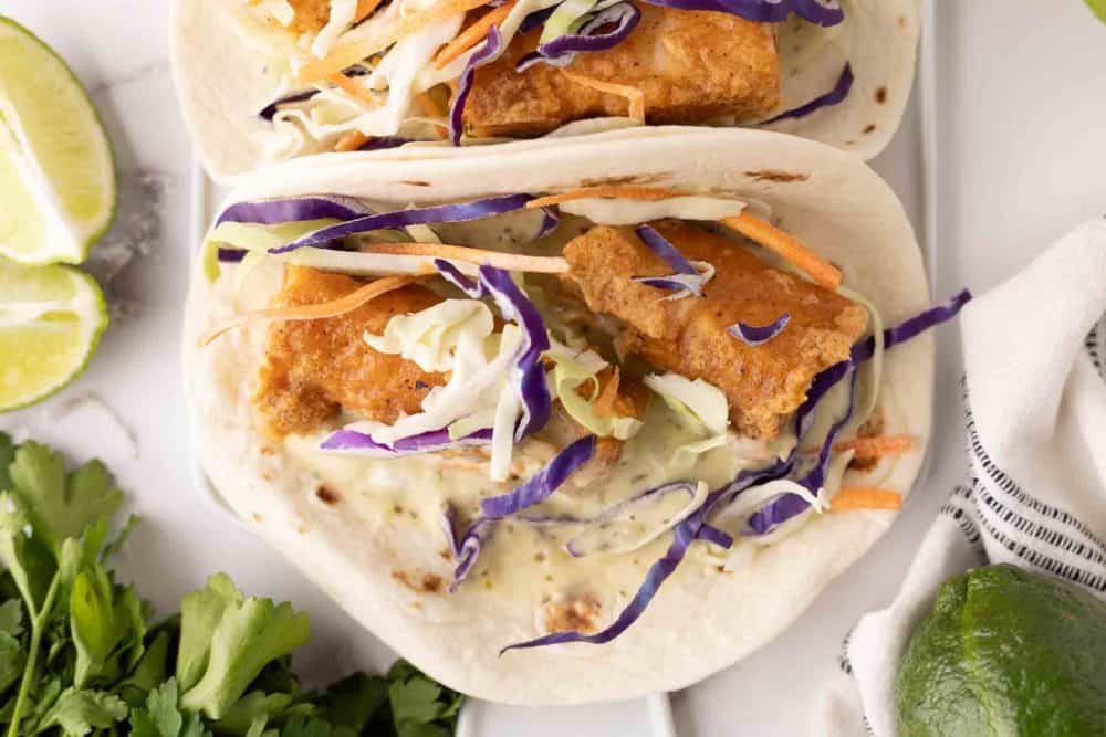 deep fried baja fish taco recipe with cabbage on a flour tortilla with limes.