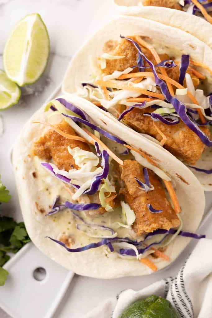 deep fried baja fish taco recipe with cabbage on a flour tortilla with limes.
