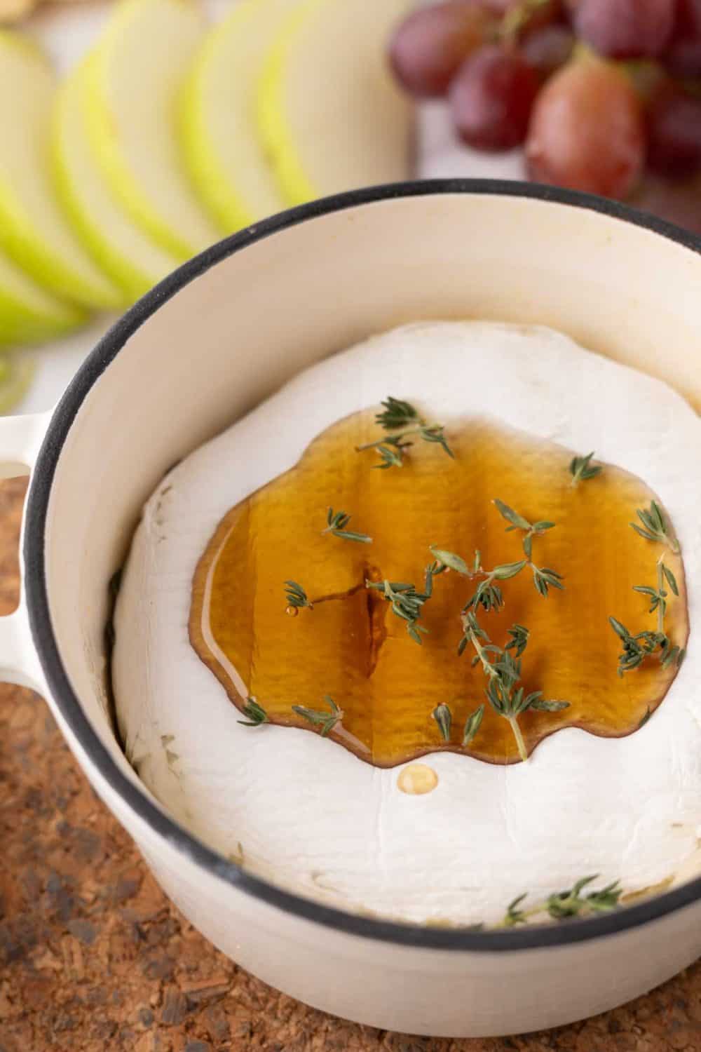 baked brie wheel in a dutch pot with thyme and honey next to crackers and fruit.