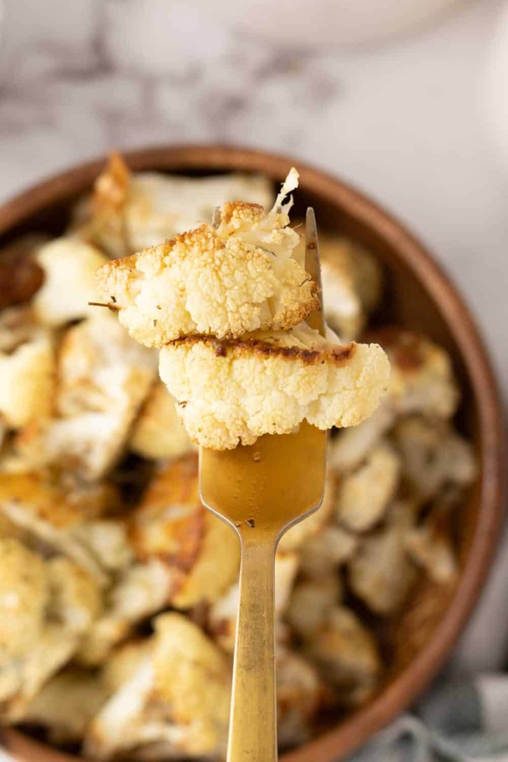 baked cauliflower florets on a fork over a a wooden bowl.