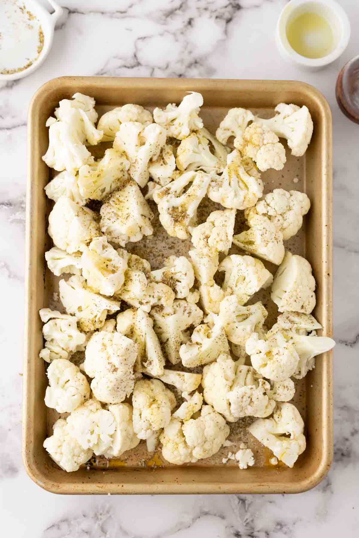 raw white cauliflower florets seasoned on a baking dish.