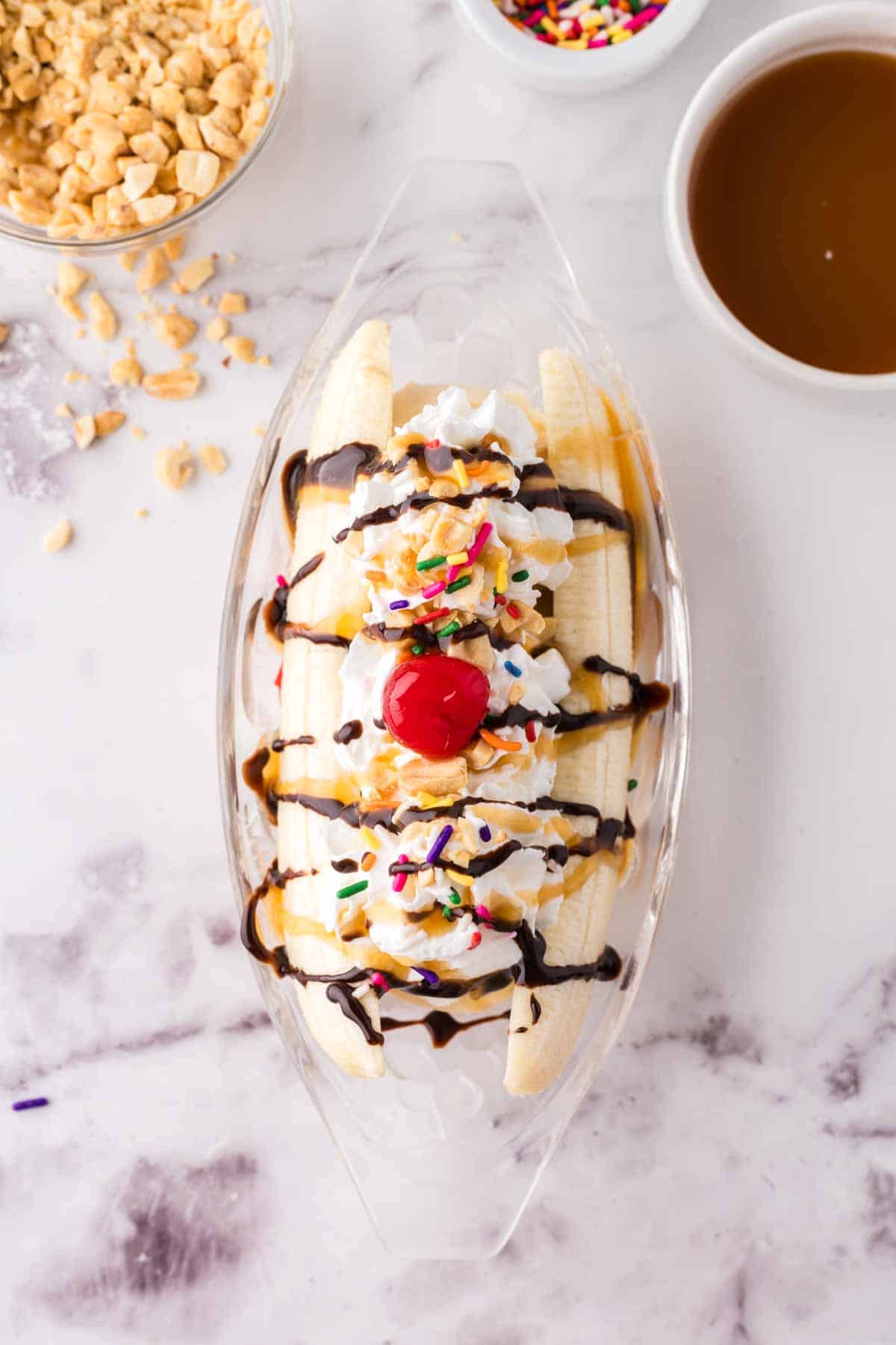 oval dish with banana split making in progress with bananas and vanilla ice cream chocolate and sprinkles.