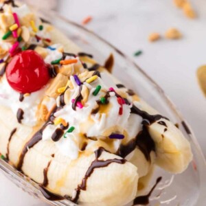 oval dish with classic banana split recipe with vanilla ice cream chocolate sprinkles and a cherry on top.