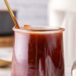 small glass jar with barbecue sauce and a golden spoon inside.