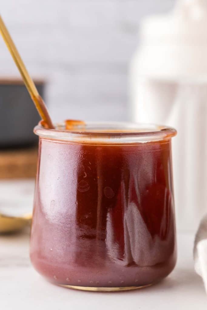 small glass jar with barbecue sauce and a golden spoon inside.
