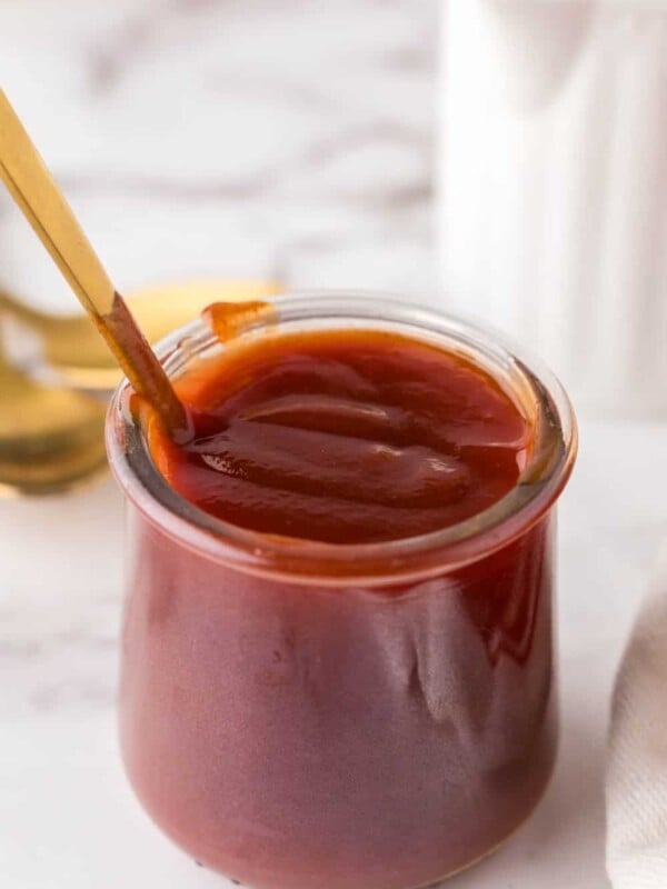 small glass jar with barbecue sauce and a golden spoon inside.