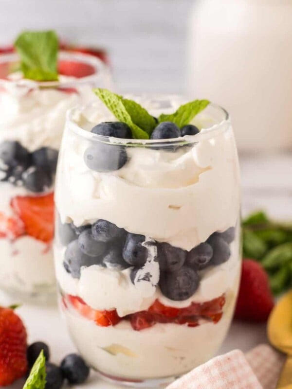 small glass with layered parfait of berries and cream with mint on top.