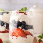 small glass with layered parfait of berries and cream with mint on top.