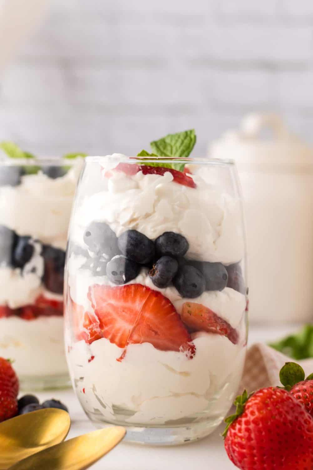 small glass with layered parfait of berries and cream with mint on top.