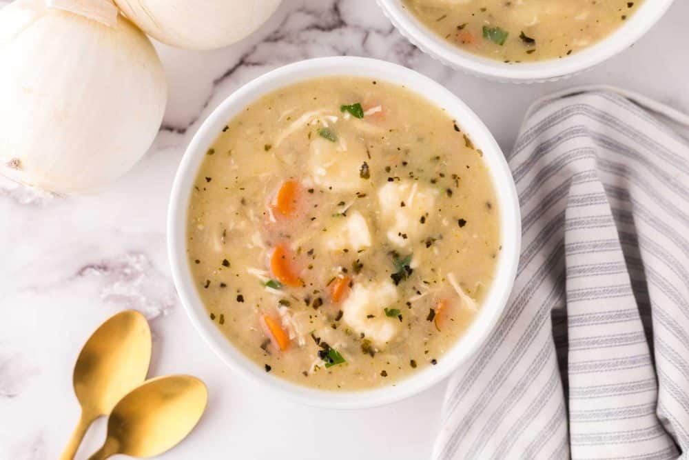bisquick dumplings recipe in white bowls with golden spoons and onions to the side.