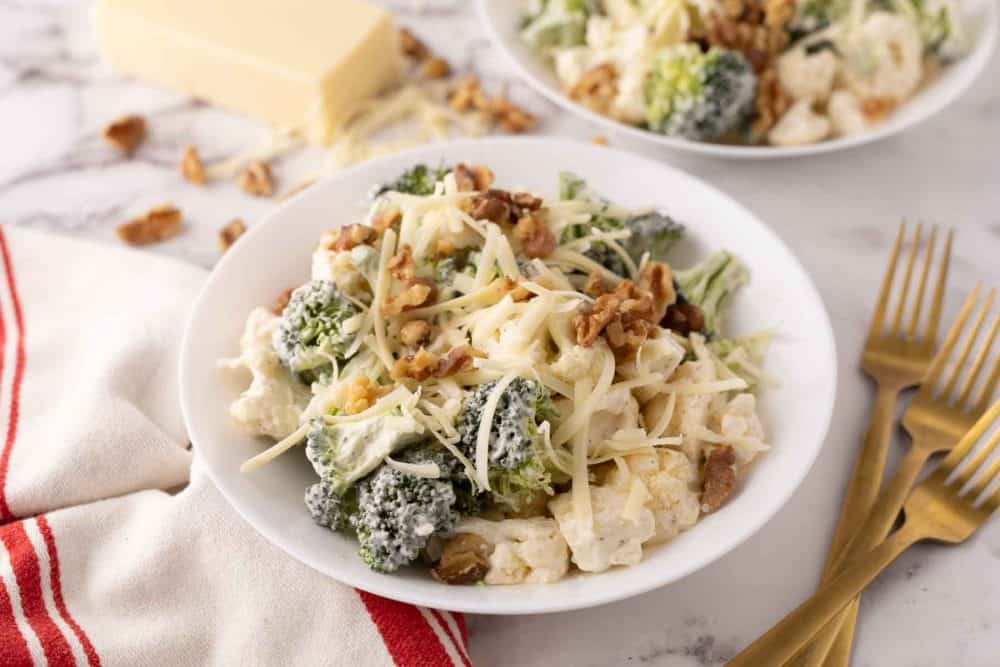 broccoli and cauliflower salad recipe with walnuts on white plates.