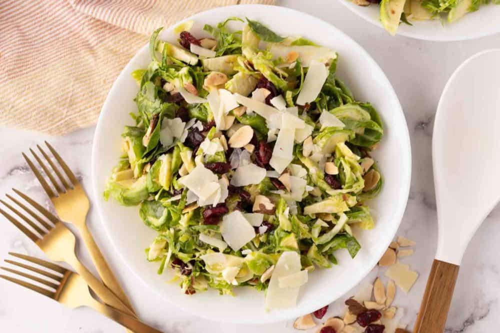 Brussels sprouts salad on a white plate with golden forks to the side.