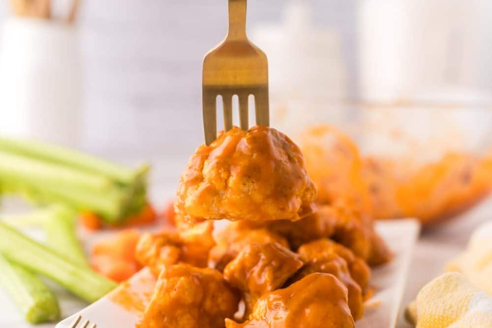 buffalo sauced cauliflower floret on a golden fork.