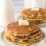 buttermilk pancakes stacked on two round plates with a pad of butter on top.