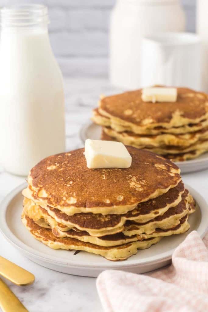 buttermilk pancakes stacked on two round plates with a pad of butter on top.