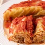 cooked cabbage rolls smothered in red sauce on a round plate sliced in half.