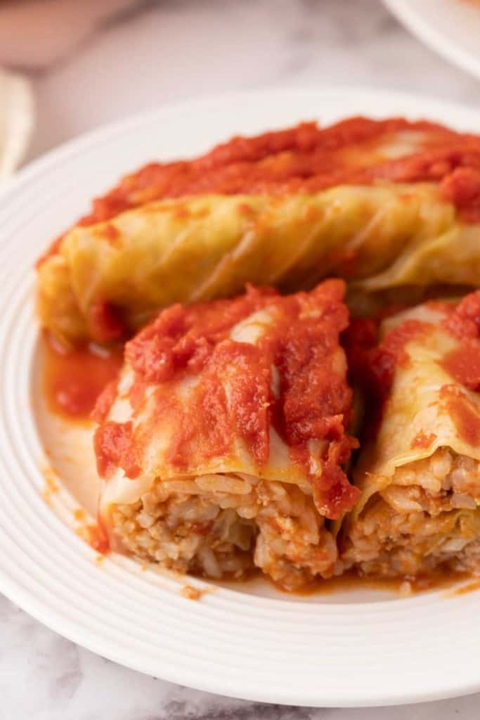 cooked cabbage rolls smothered in red sauce on a round plate sliced in half.
