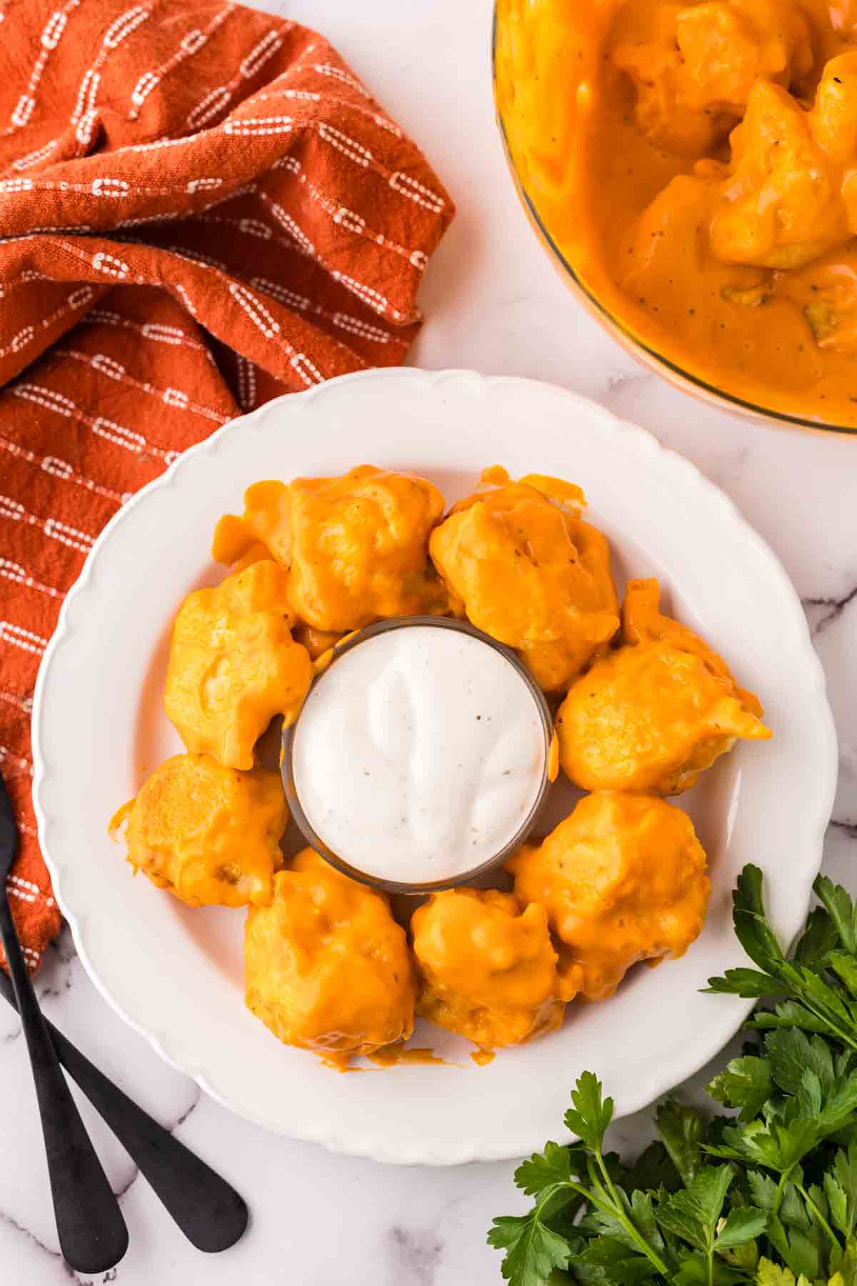 cauliflower wings in a ring around a dish of dipping sauce on a round plate.