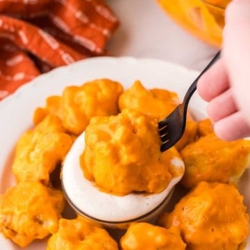 cauliflower wings in a ring around a dish dipping sauce with one on a fork POV dipped in.