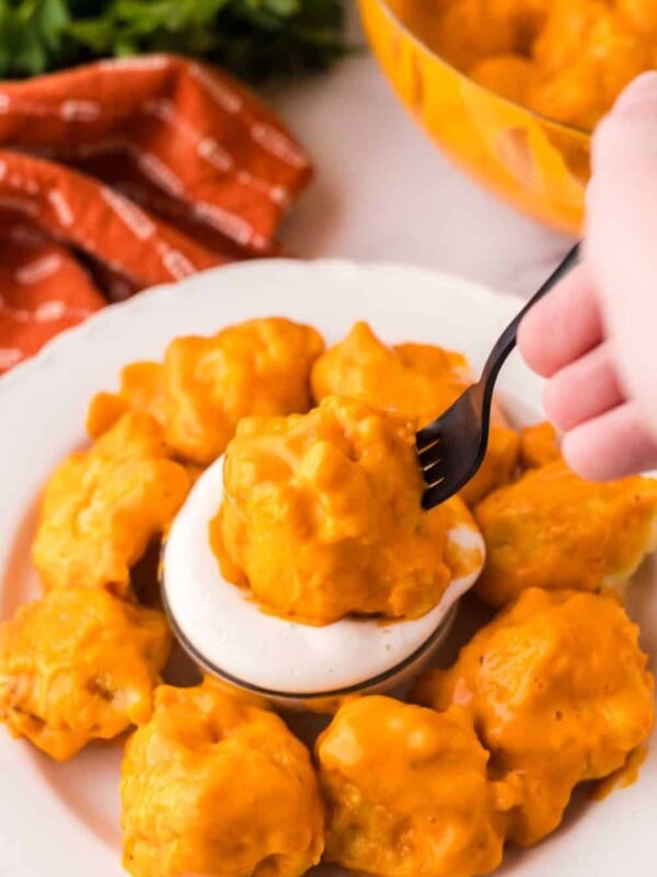 cauliflower wings in a ring around a dish dipping sauce with one on a fork POV dipped in.