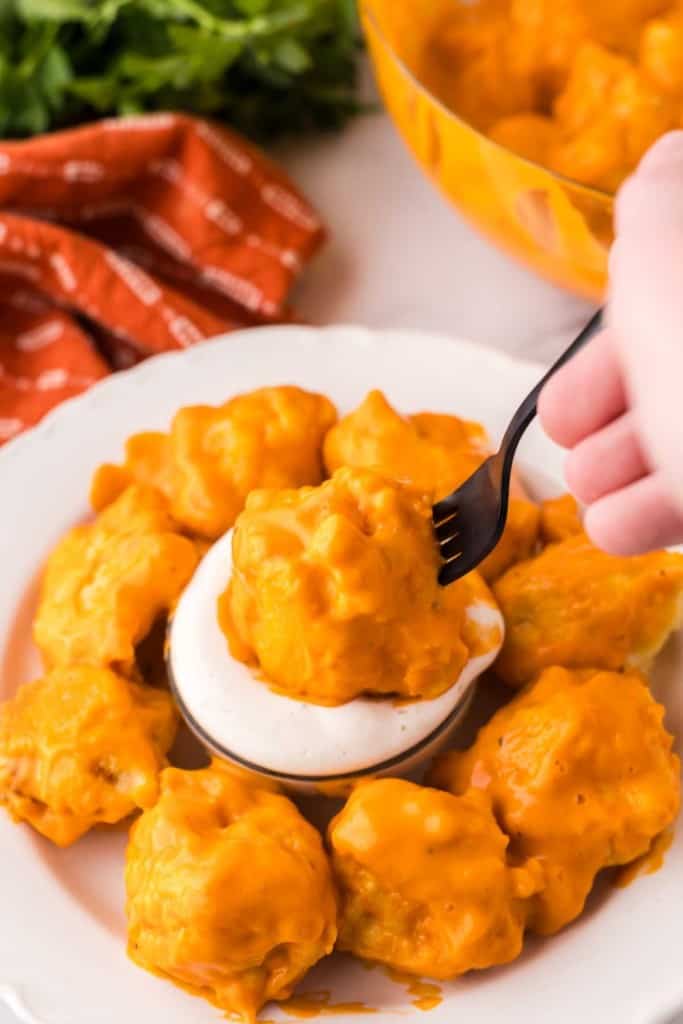cauliflower wings in a ring around a dish dipping sauce with one on a fork POV dipped in.