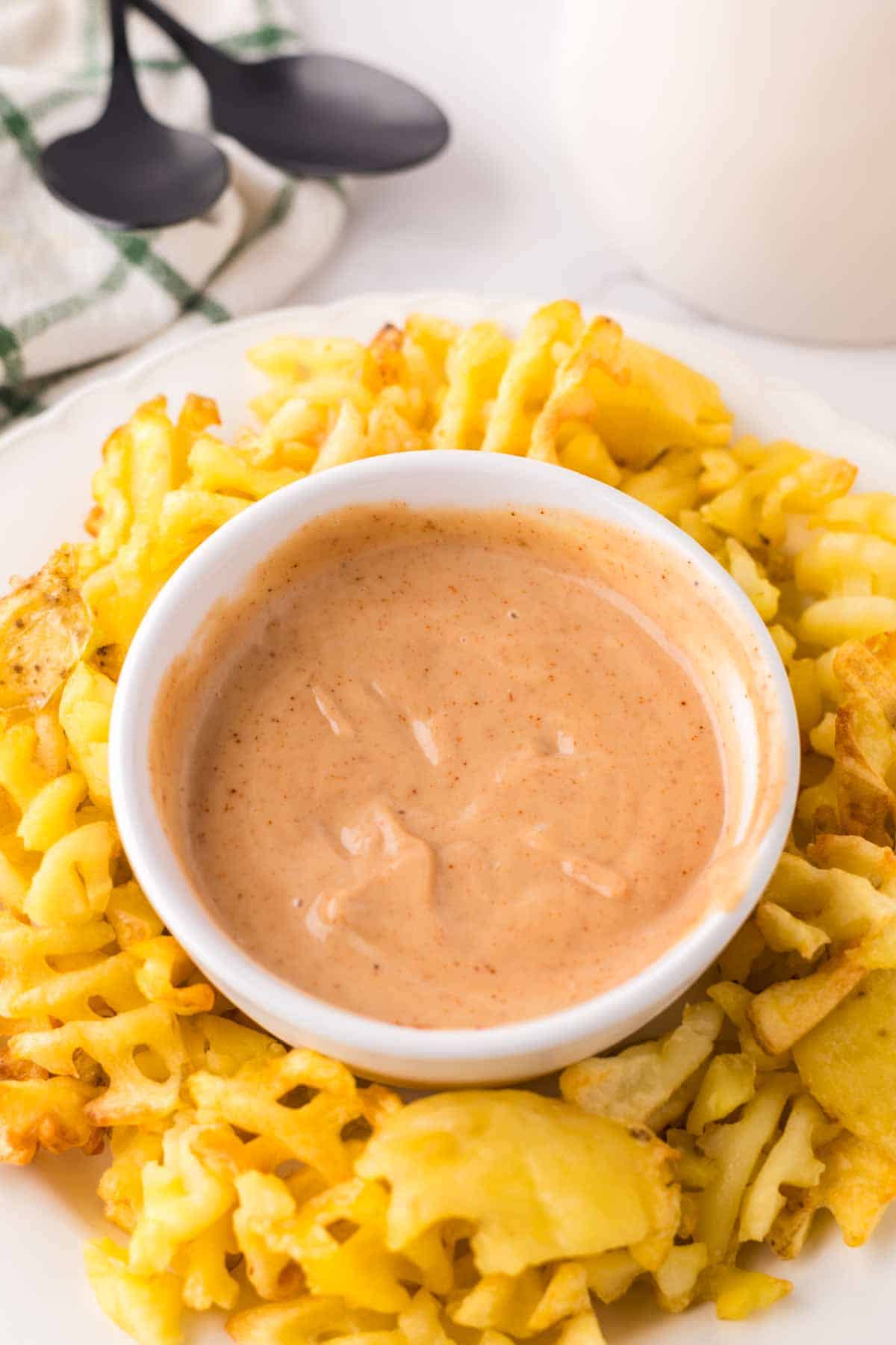 Chick-fil-A Sauce in a small bowl with waffle fries all around on a round plate.