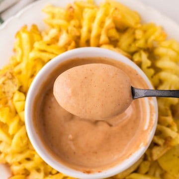 Chick-fil-A Sauce spooned out of a small bowl with waffle fries all around on a round plate.