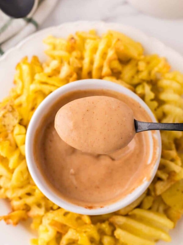 Chick-fil-A Sauce spooned out of a small bowl with waffle fries all around on a round plate.