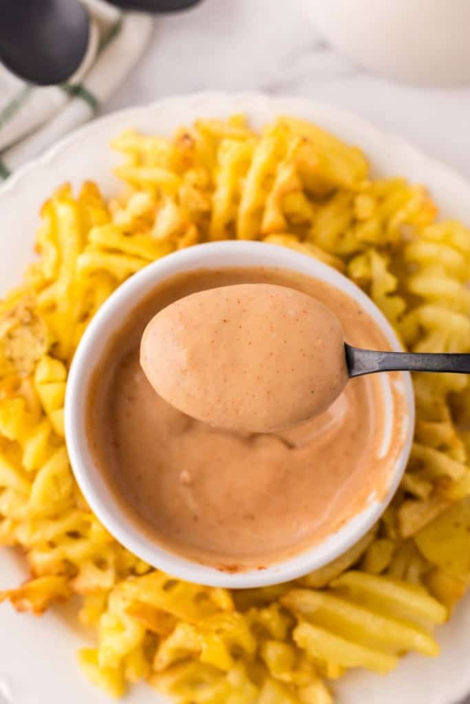Chick-fil-A Sauce spooned out of a small bowl with waffle fries all around on a round plate.