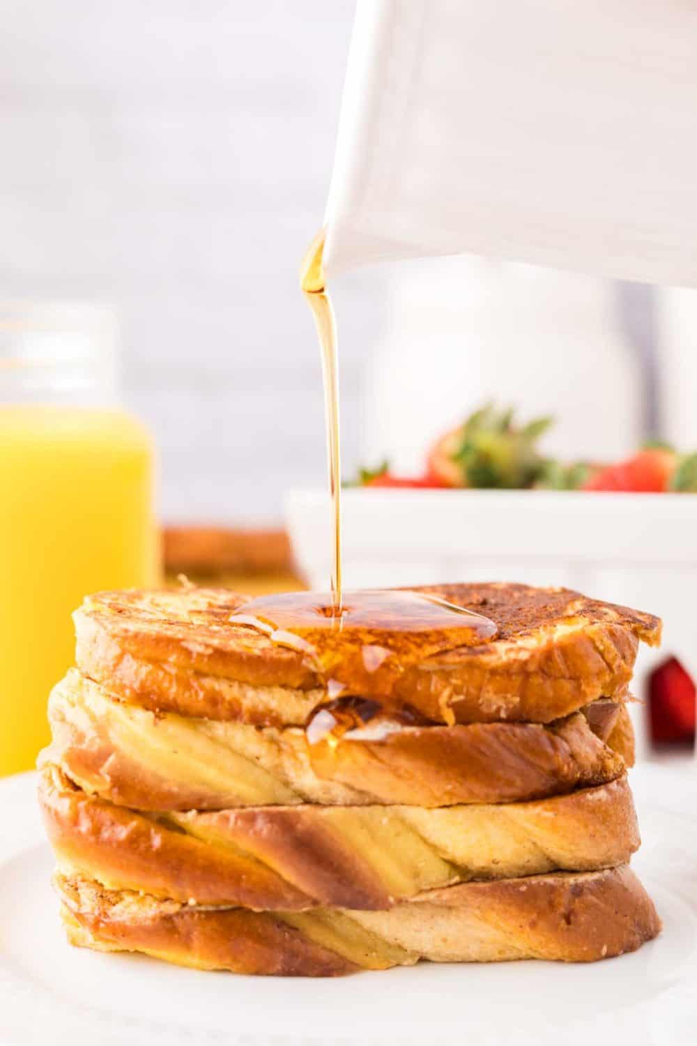 stack of four pieces of challah french toast on a plate with syrup dripped on top.